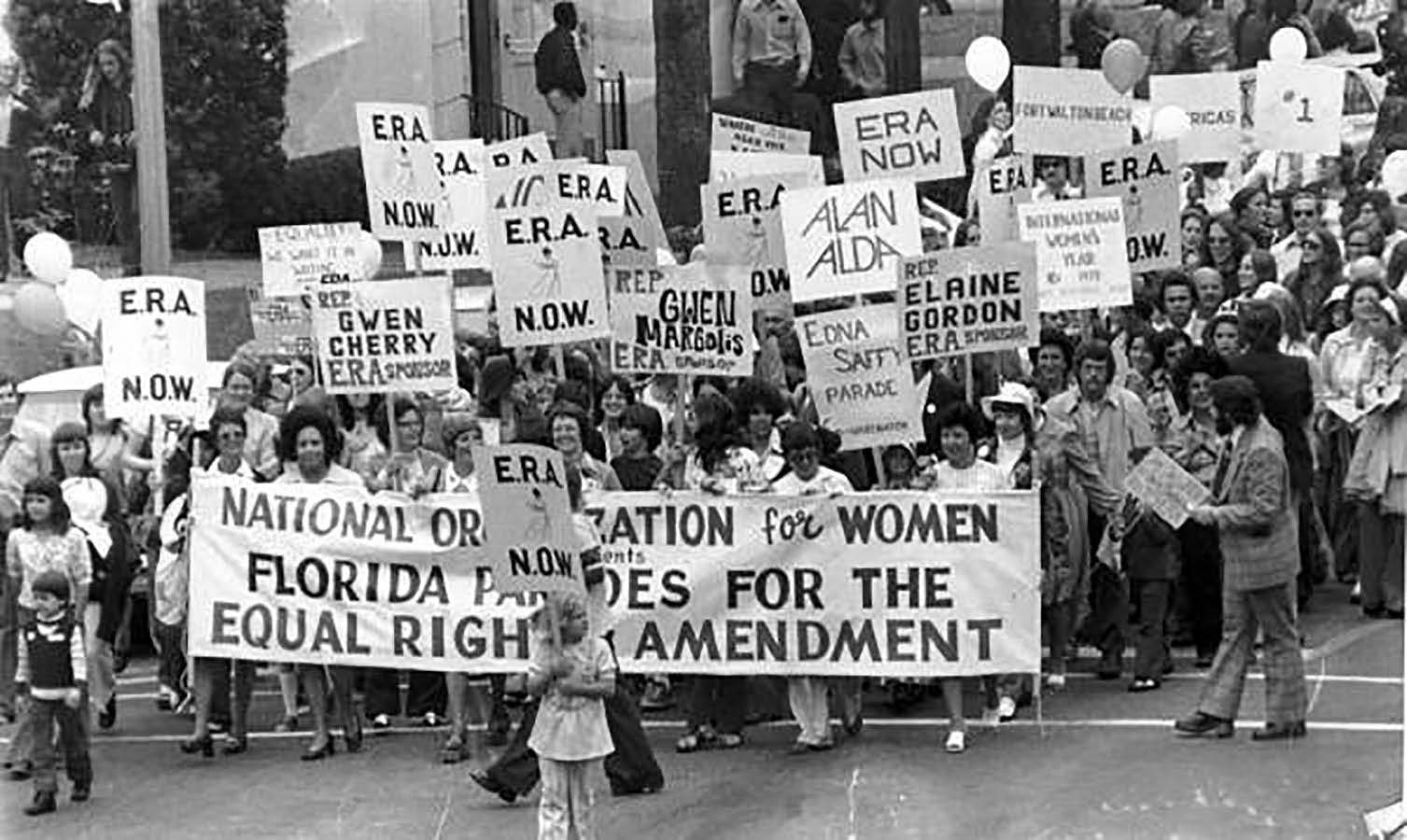 A black-and-white photo of a large group of woman holding signs, many saying ERA, and marching down a street.
