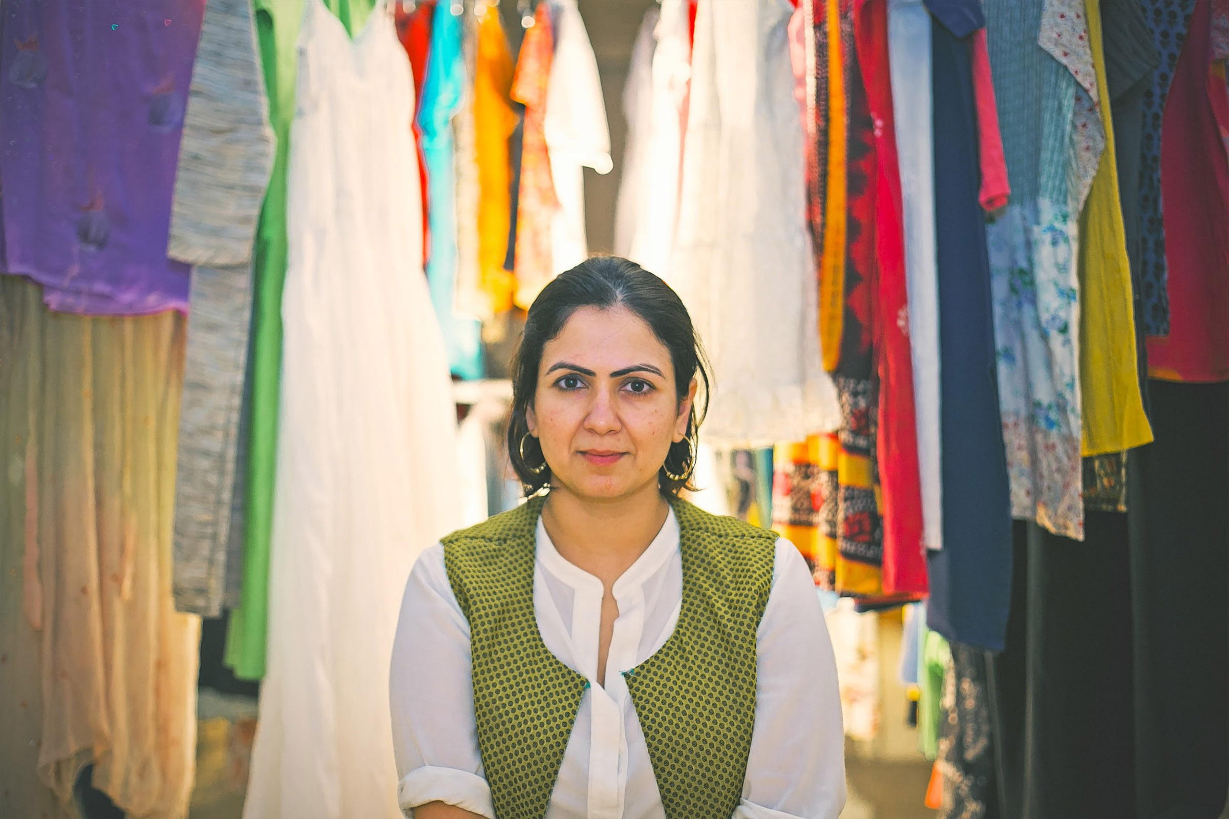 A woman looking at the camera standing in front of draped multi-color clothing.