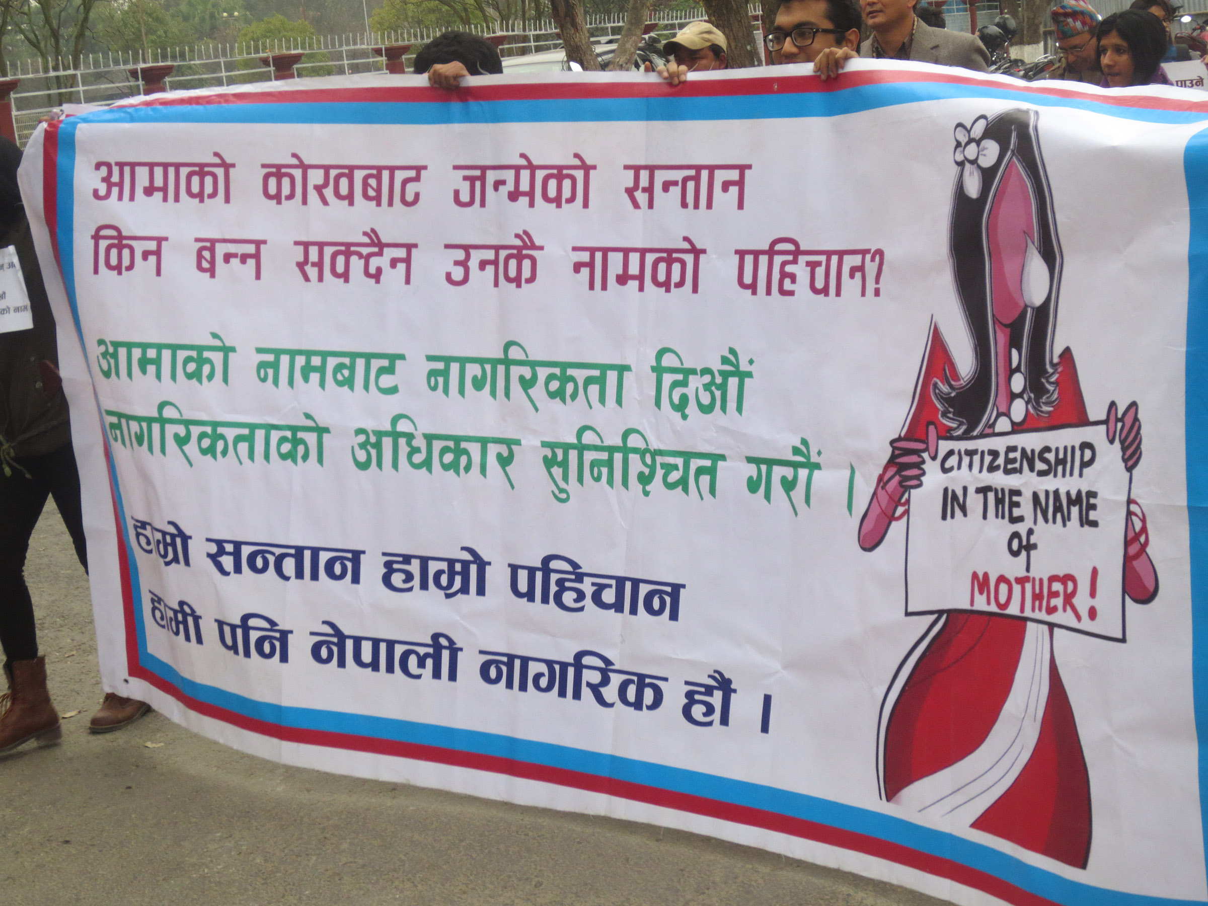 Nepali people hold a large white banner with Nepali writing on it, with the design of a woman with a tear holding a sign that says "Citizenship in the name of the Mother!"