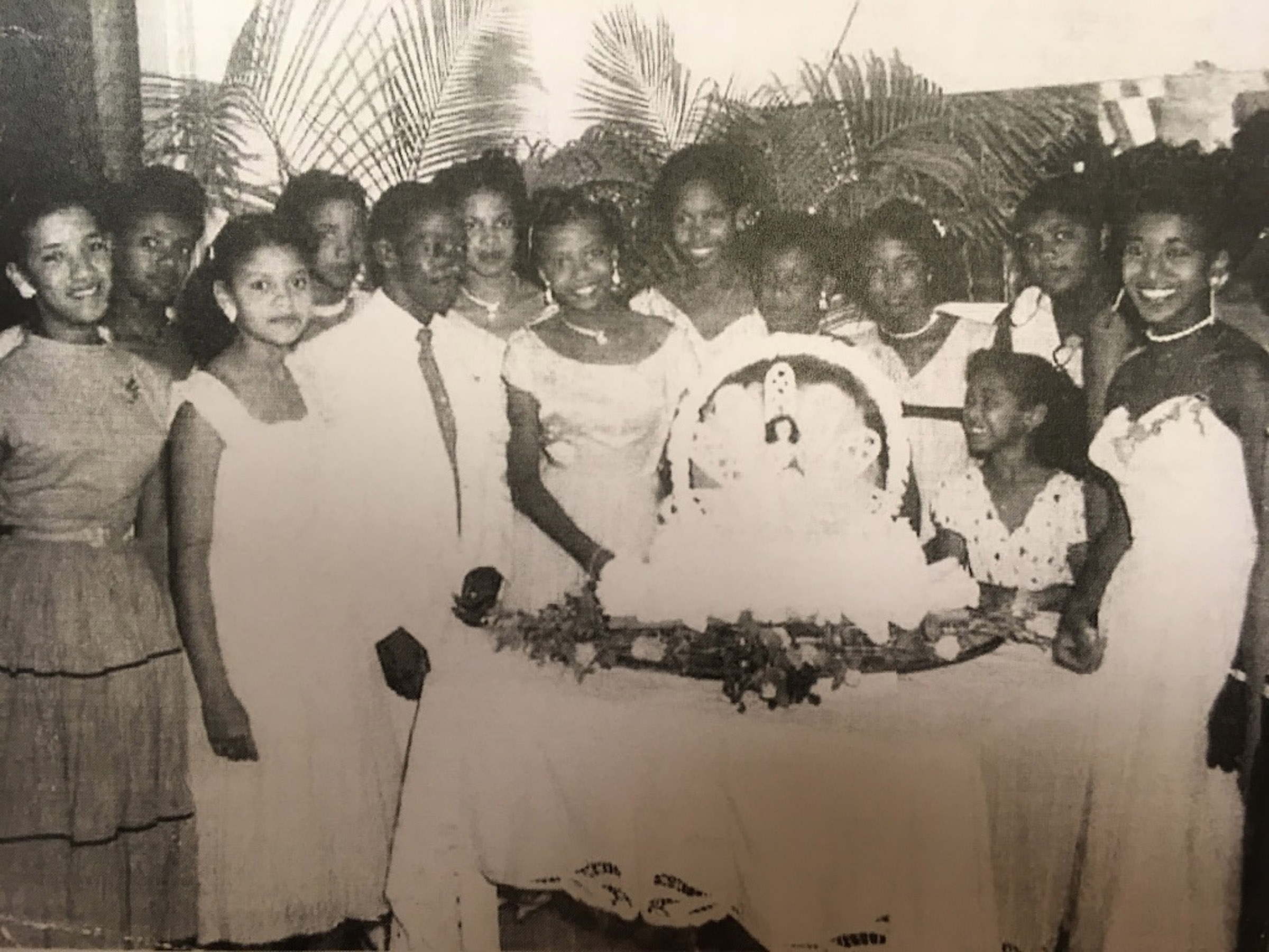 A black-and-white photo of a group of well-dressed men and women in front of a lavish cake.