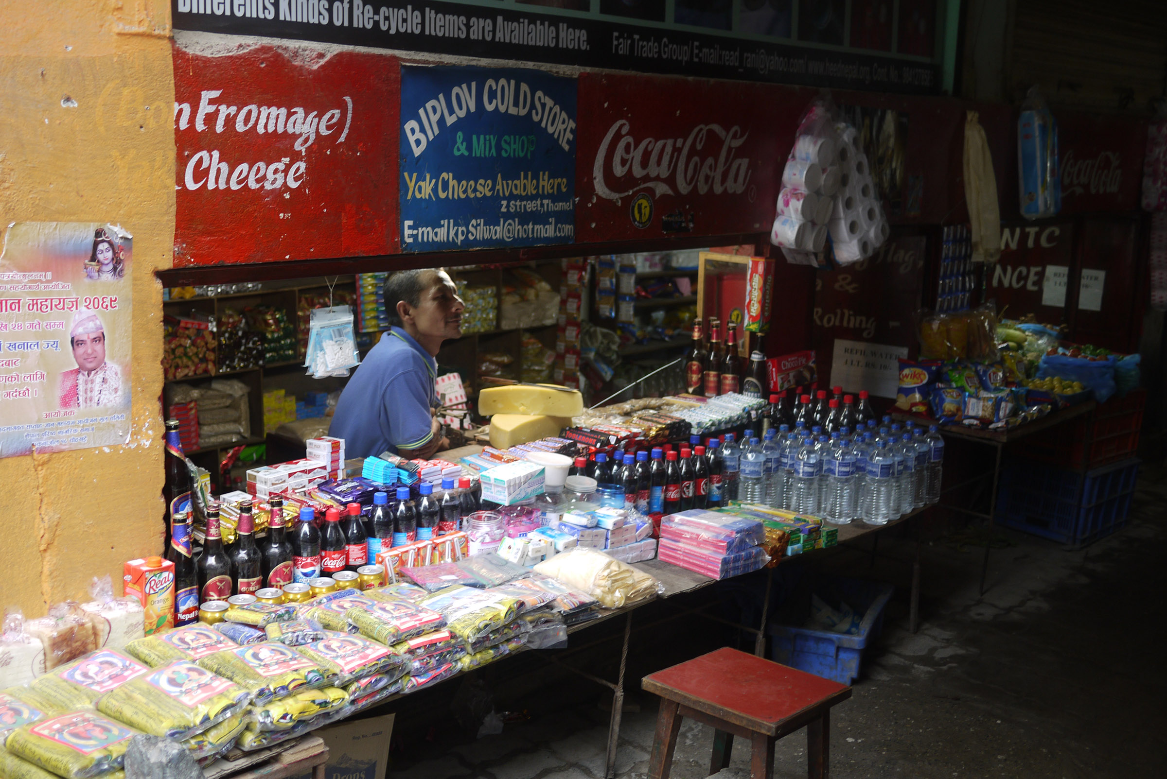 A shopkeeper looks over his counter, filled with Coca Cola products and other packaged items.