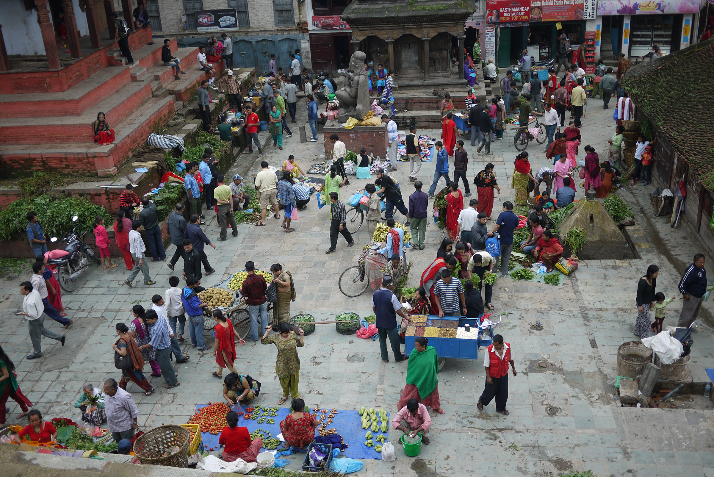 A top-down view of a large market filled with people walking between blankets spread with produce and other goods.