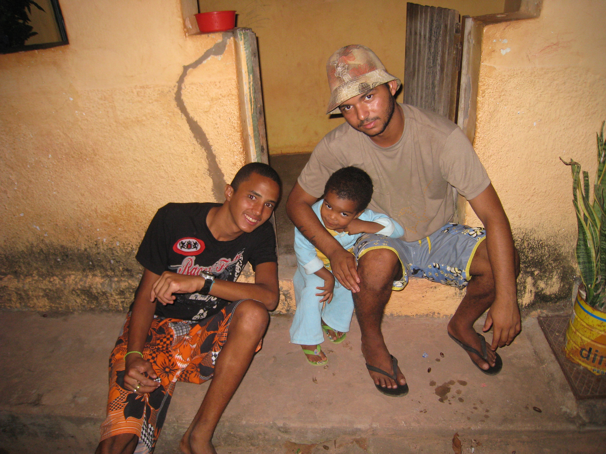 Two boys and a young man sit outside a rural building, smiling.