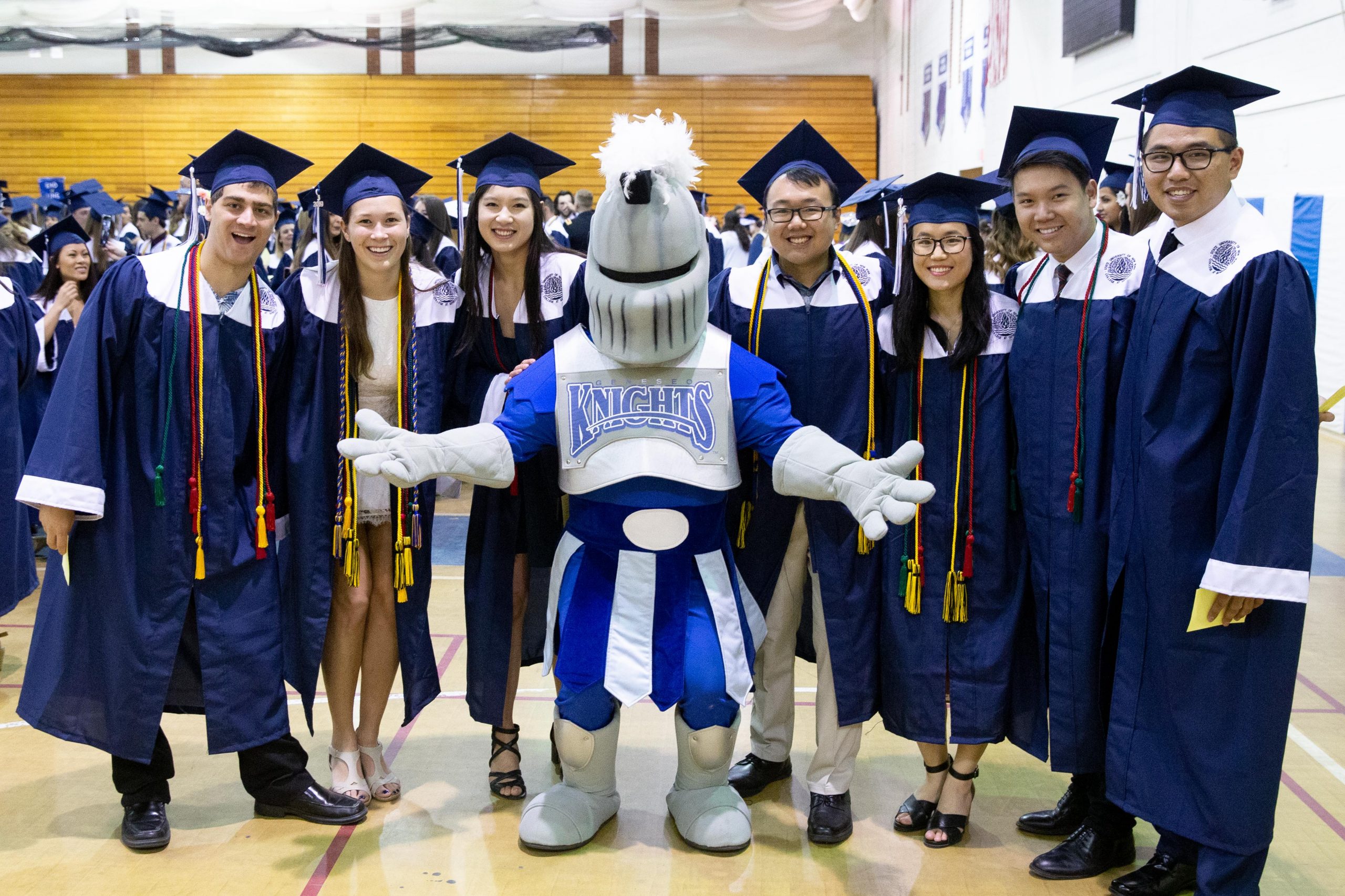 College graduates in robes and mortar board hats pose for a picture with the school mascot, a knight.