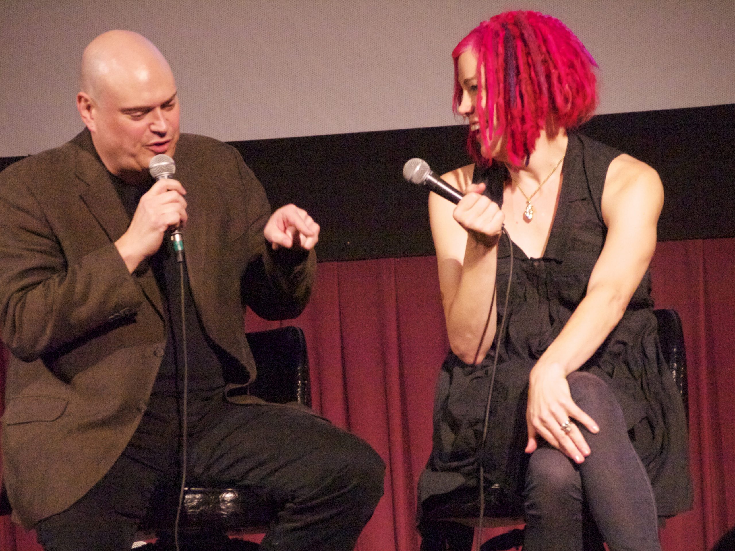 Two people sit next to each other holding microphones.