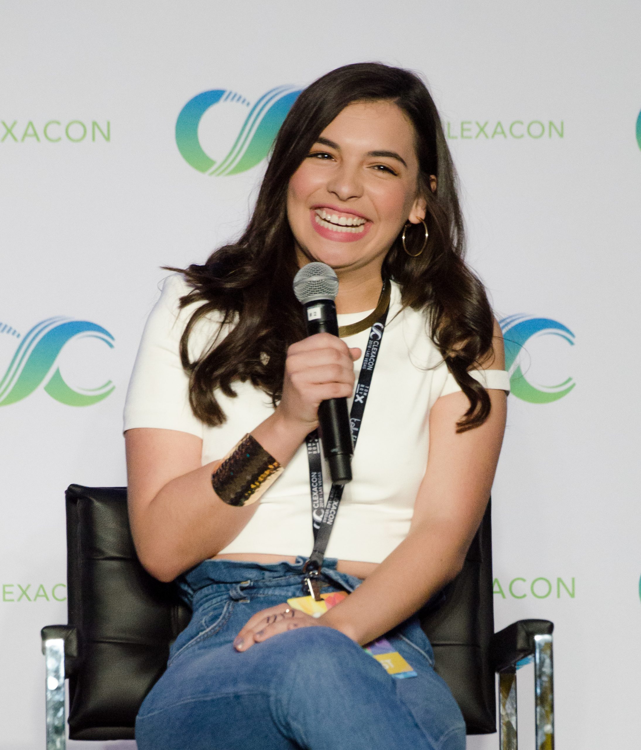 A woman sits in a chair and laughs holding a microphone.