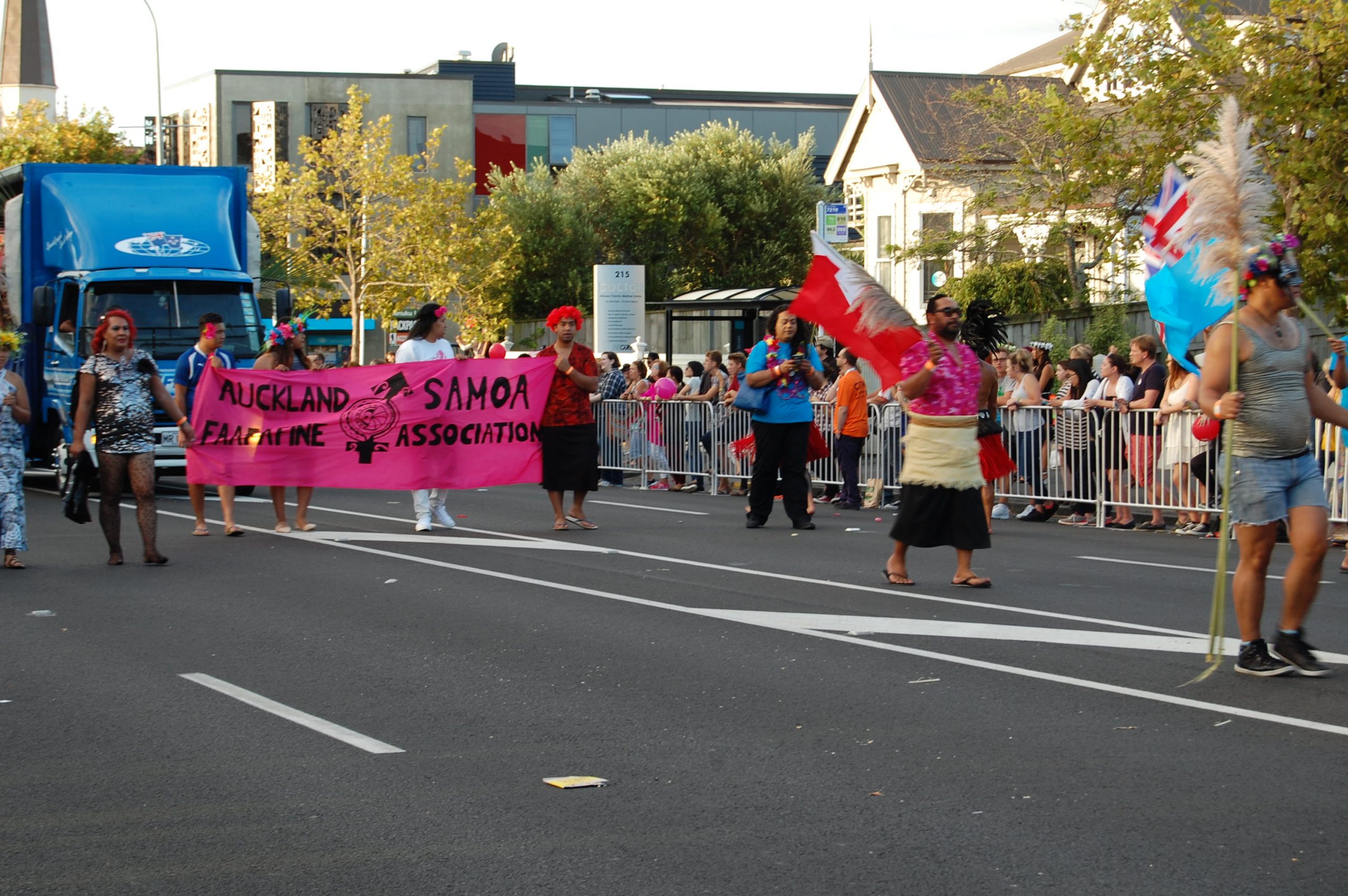 A parade, line of people hold a sign that says "Auckland Samoa Fa'afafine Association."