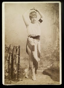 Old photograph of a man in a dress with his hands raised.