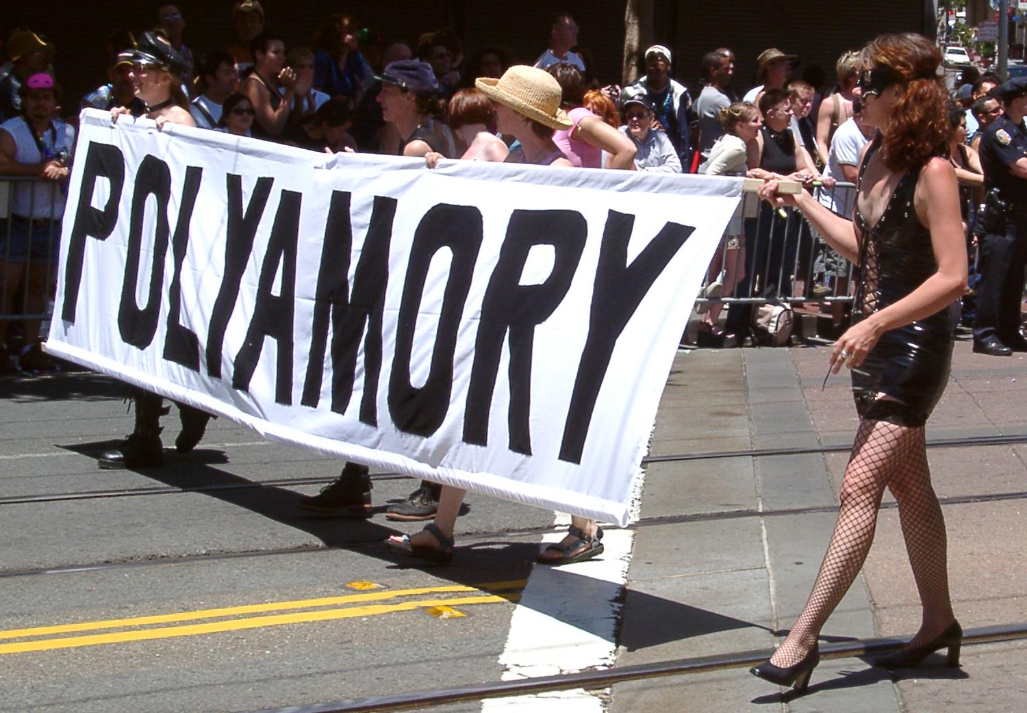 A line of people hold a banner that says "POLYAMORY."