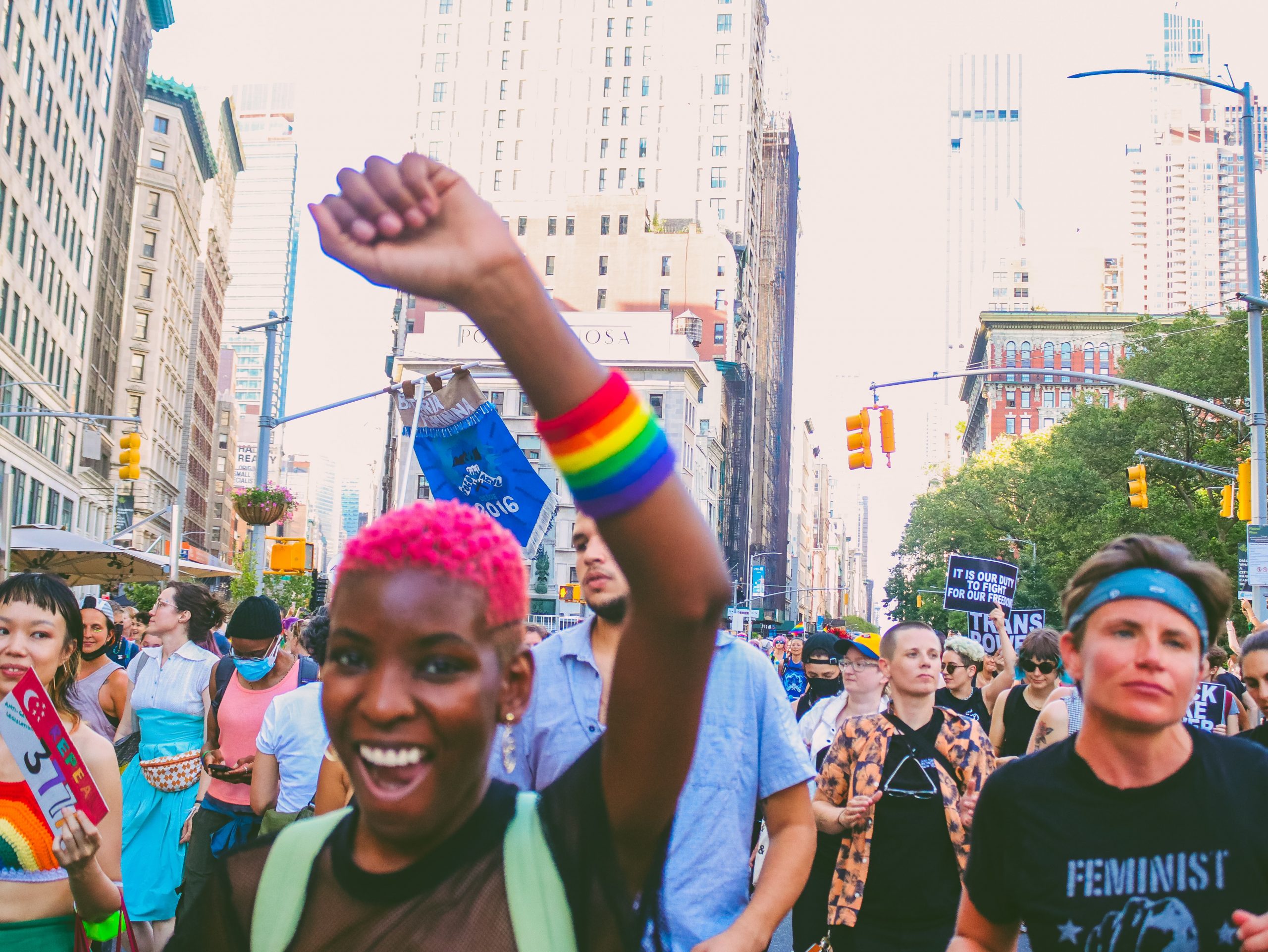 A pride parade, a person holds their fist up with a rainbow wristband.