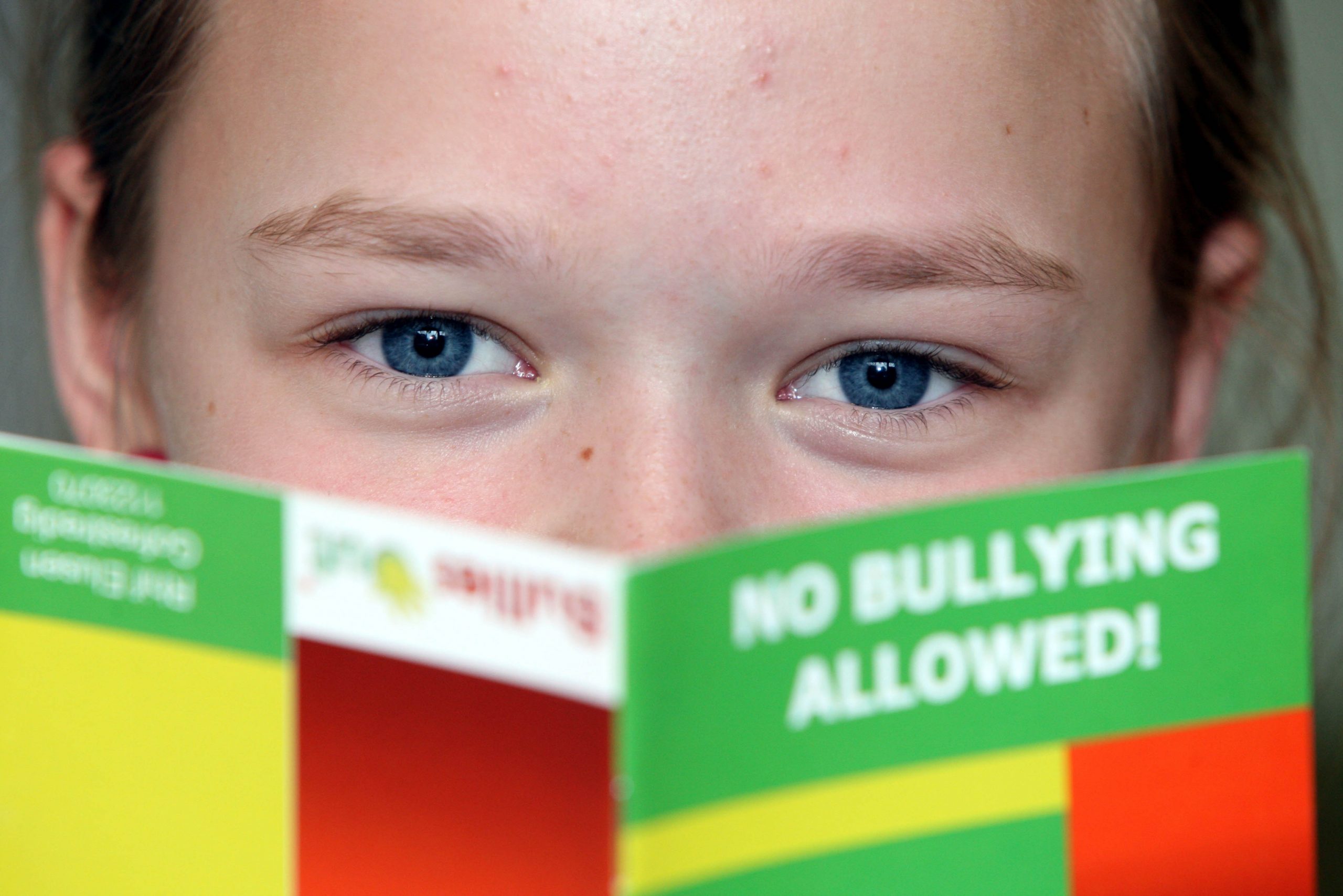 A child looks up from a pamphlet that says "NO BULLYING ALLOWED!"