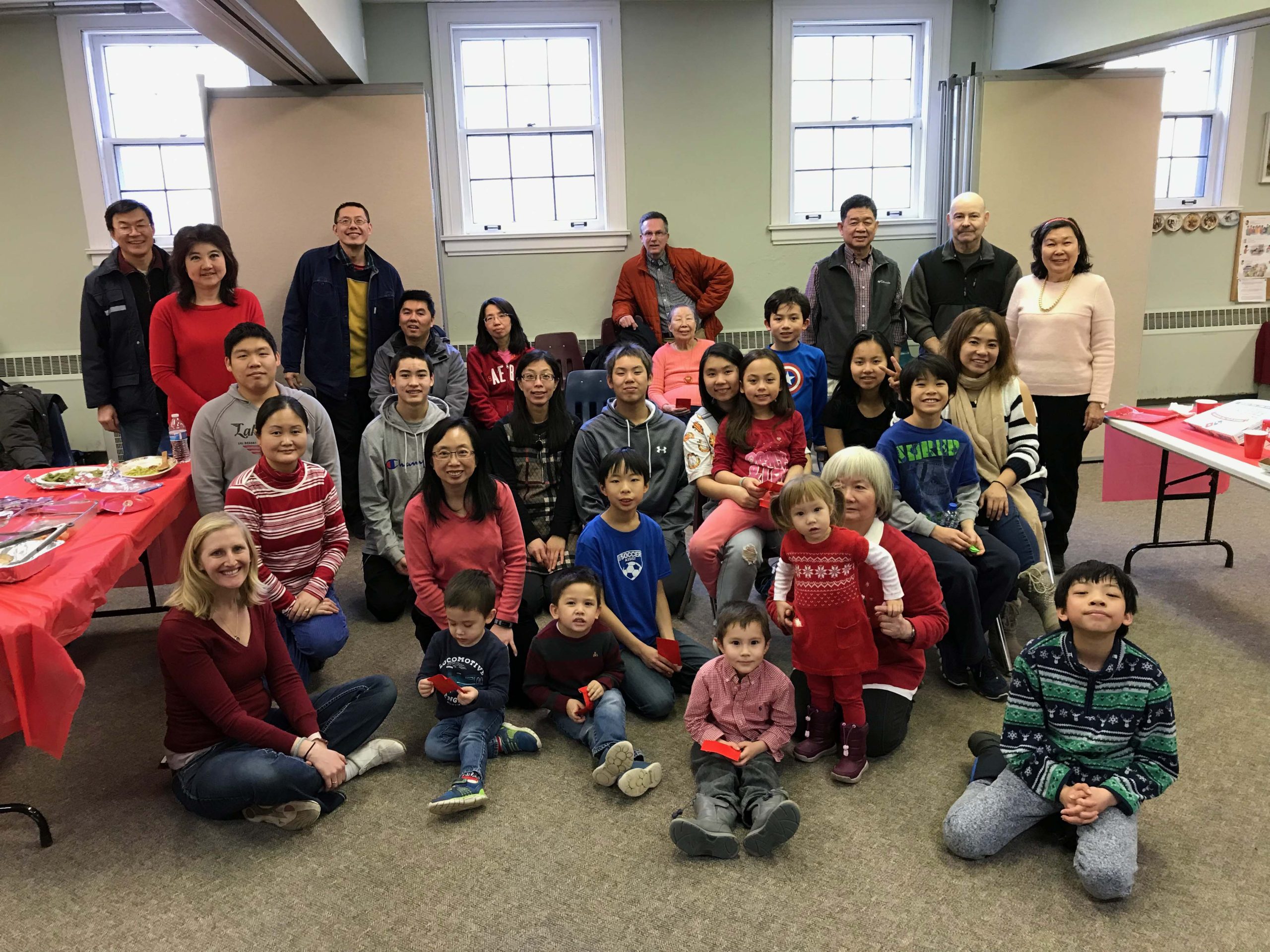 A group of people and children sit in a room, smiling.