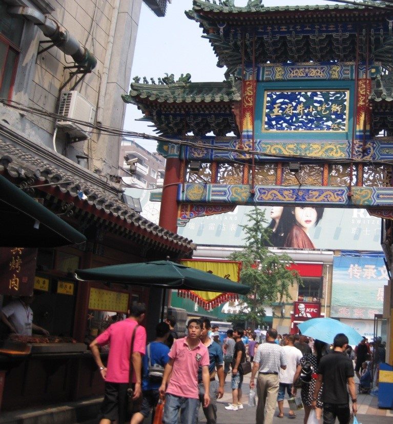 A group of people walk down a street under an elegant archway.