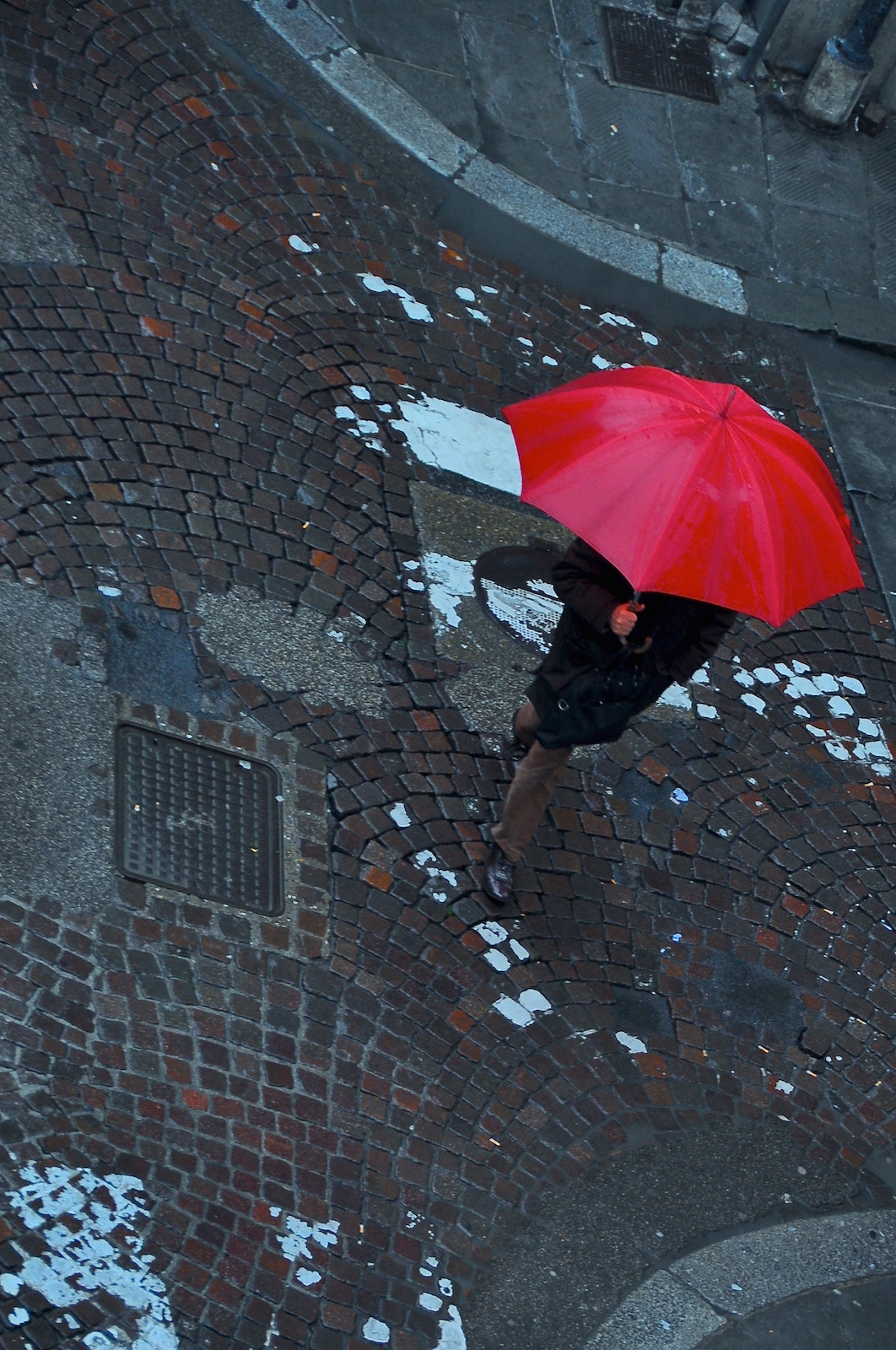 A person walks on a rainy street with a red umbrella.