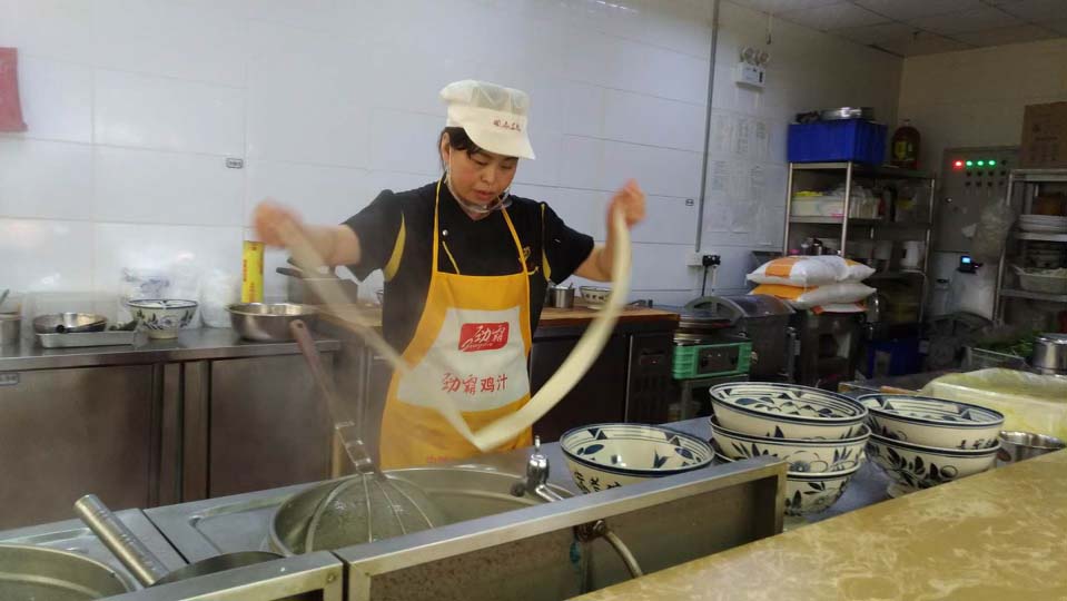 A women stretches dough in front of a stove and multiple bowls.