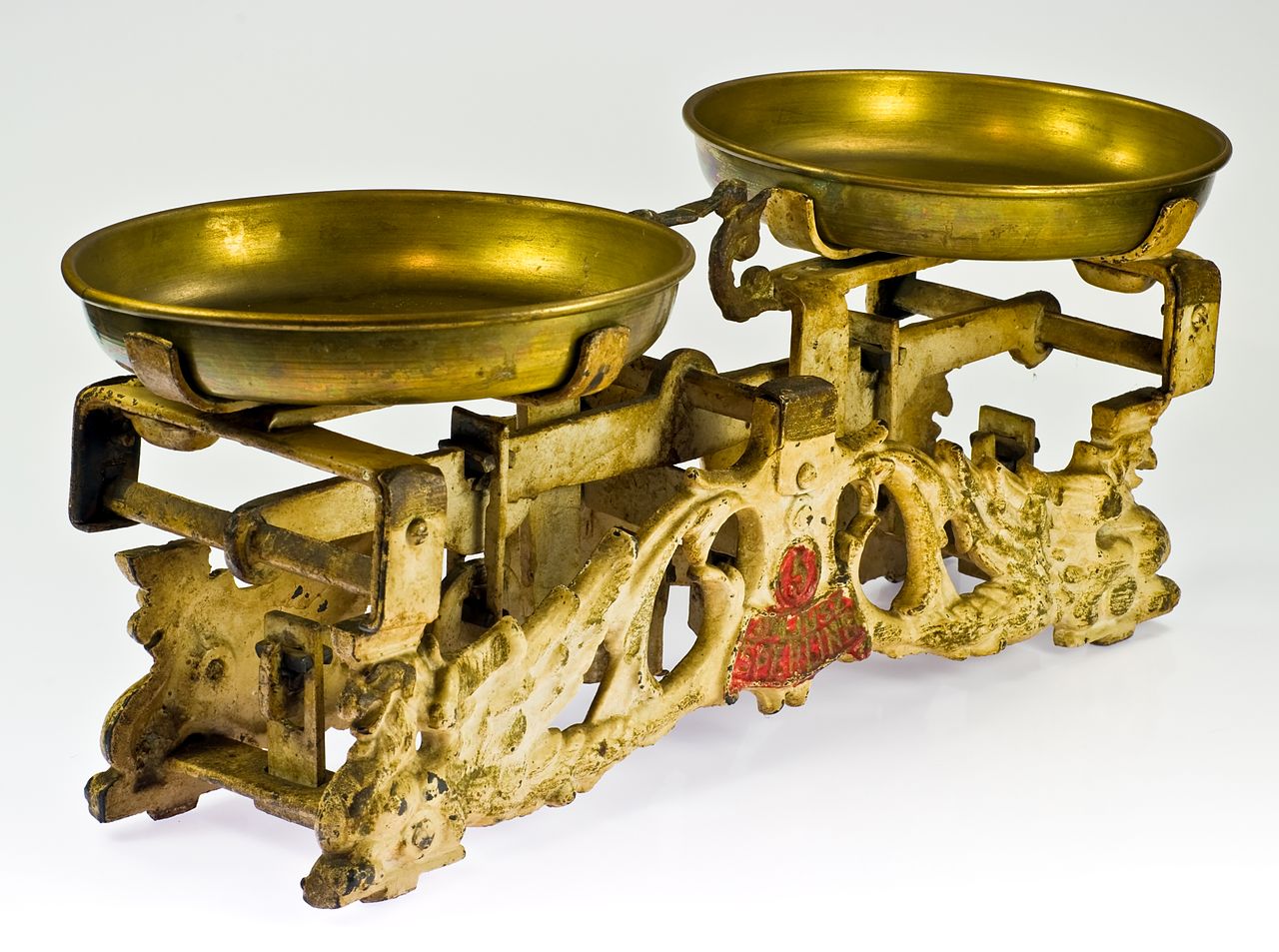 Vintage balance scale with two brass pans on an ornate, weathered iron base.