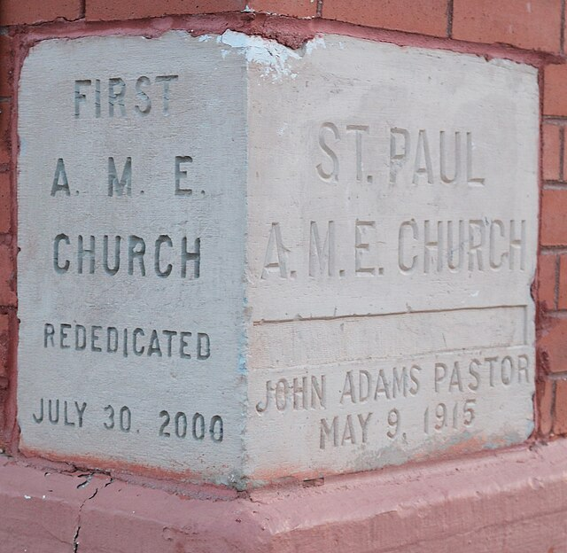 Cornerstone of a red brick church with engraved text: "First A.M.E. Church, Rededicated July 30, 2000" and "St. Paul A.M.E. Church, John Adams Pastor, May 9, 1915."