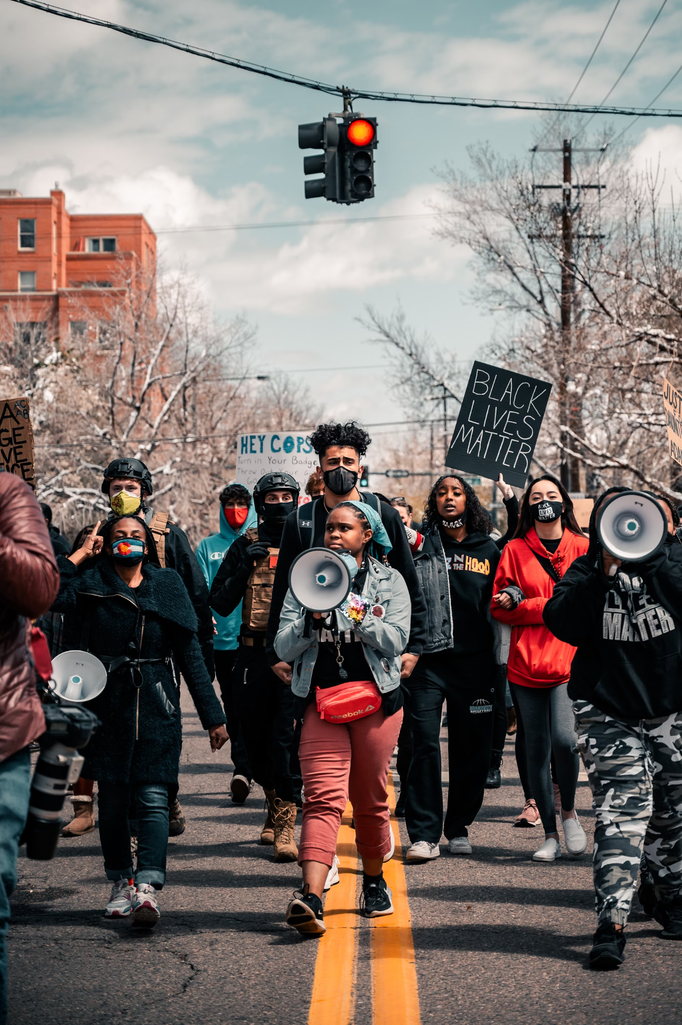 A group of protesters marches peacefully under a red traffic light. People hold "Black Lives Matter" signs and megaphones.