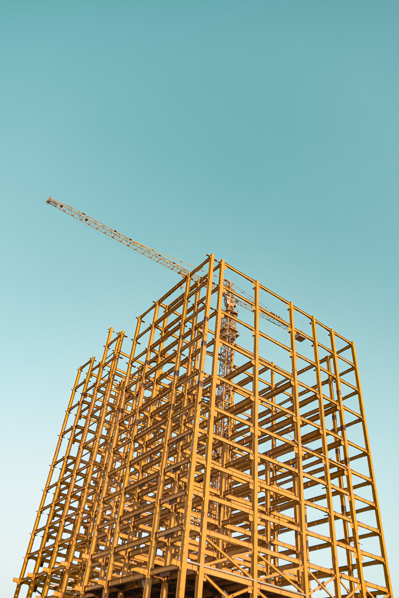 A towering yellow steel framework of a building under construction against a clear blue sky, with a crane extending from its center, symbolizing growth.