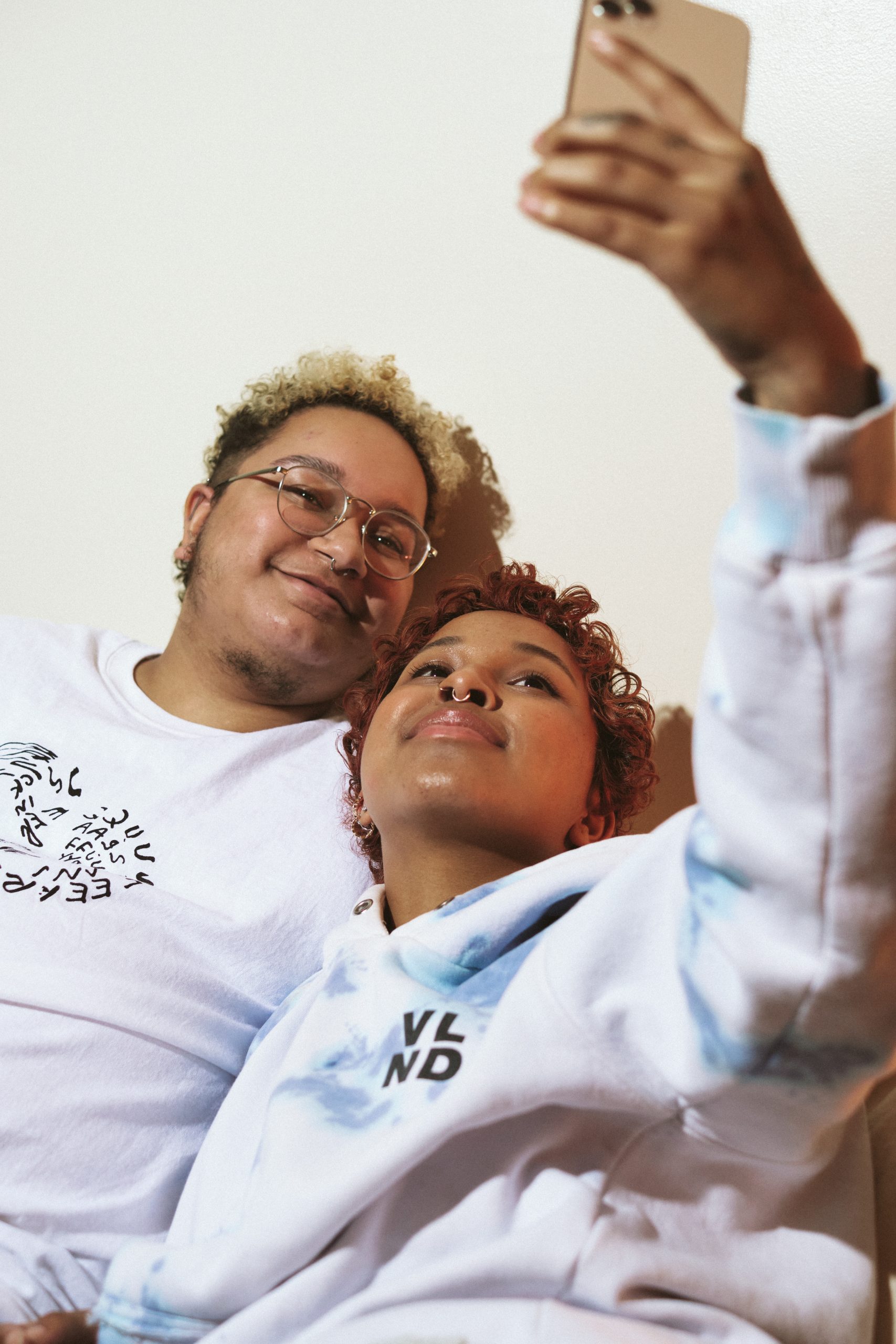 Two trans people smiling and taking a selfie together. Both wear casual clothes and appear relaxed and happy.